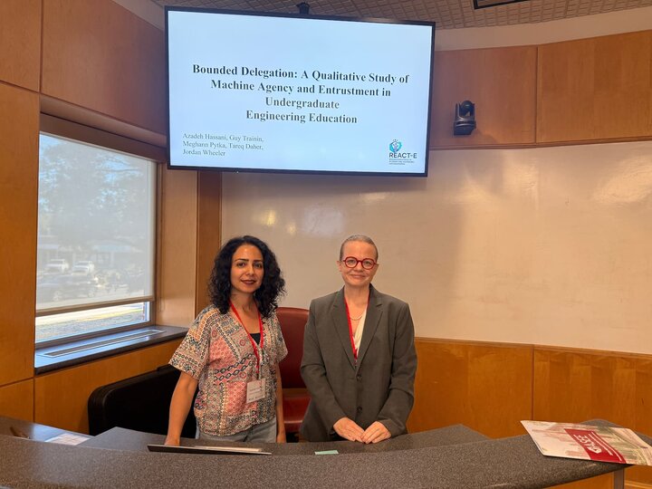 Two women standing in front of a presentation screen in a lecture room.