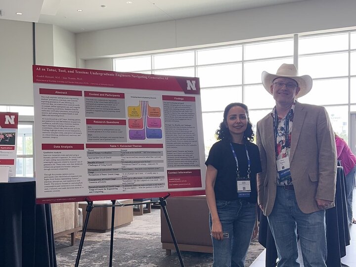 Two people smiling near a red and white academic poster on display in a bright conference room.